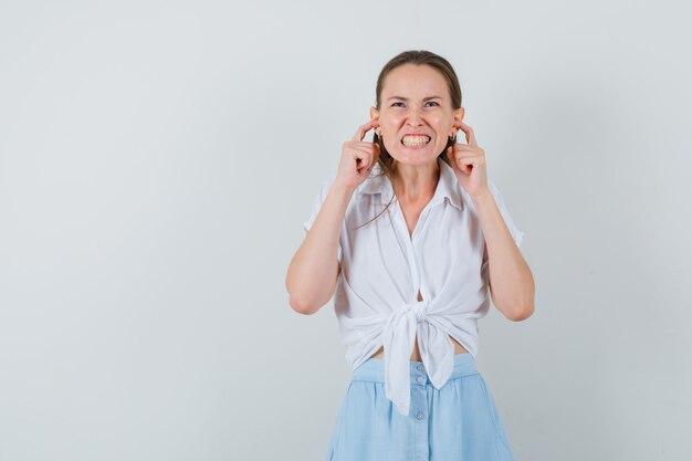 Jeune femme se bouchant les oreilles avec les doigts en chemisier, jupe et à l'ennui