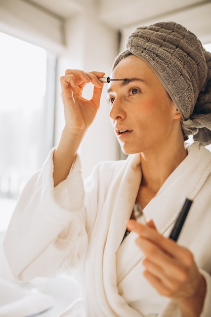 Jeune femme se brossant les sourcils et regardant dans le miroir