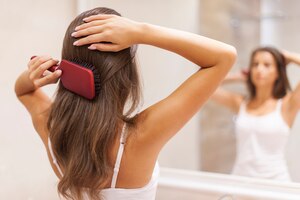 Jeune femme se brosser les cheveux sains devant un miroir