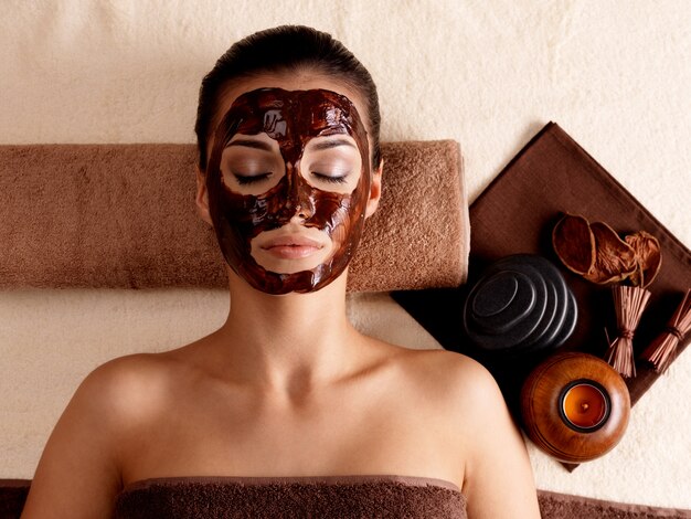 Jeune femme se détendre avec un masque facial sur le visage au salon de beauté - à l'intérieur