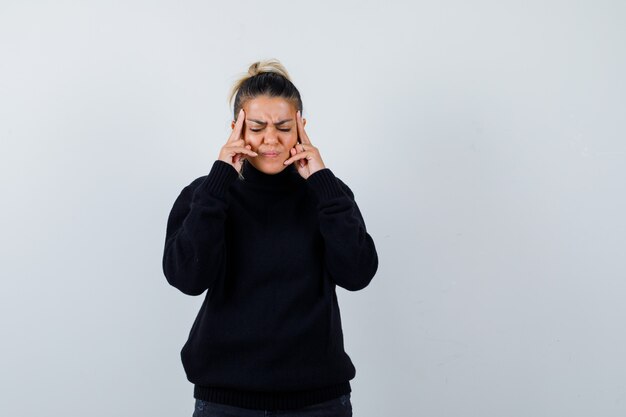 Jeune femme se frottant les tempes en pull à col roulé noir et à la fatigue. vue de face.