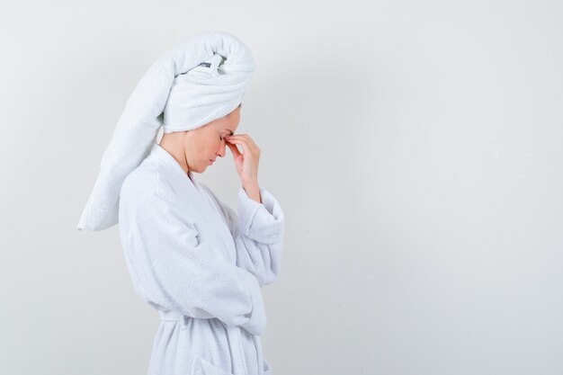 Jeune femme se frottant les yeux et le nez en peignoir blanc, serviette et à la fatigue.