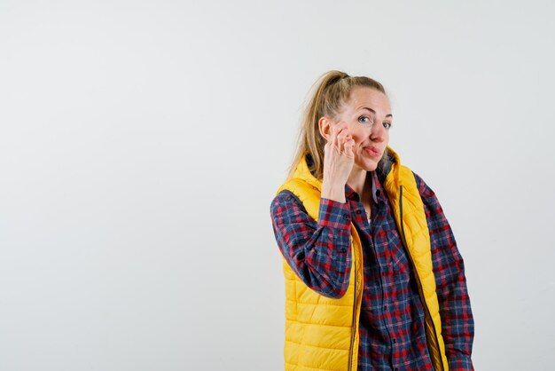 La jeune femme se gratte la joue sur fond blanc