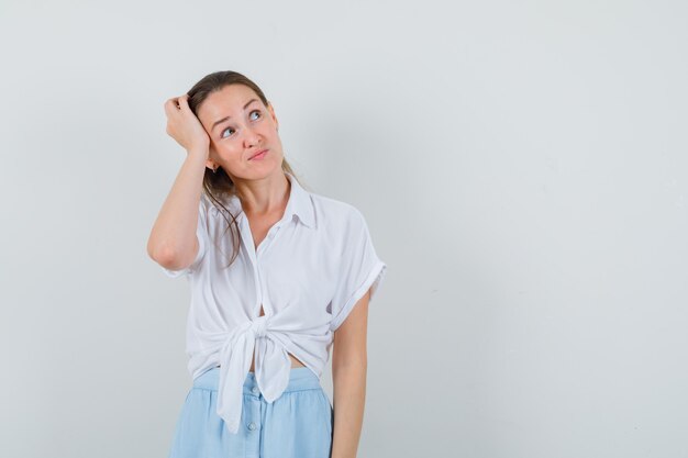 Jeune femme se gratter la tête en chemisier et jupe et à hésiter