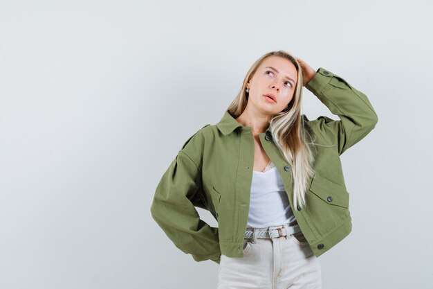 Jeune femme se gratter la tête dans la veste, le pantalon et à la vue pensive, avant.