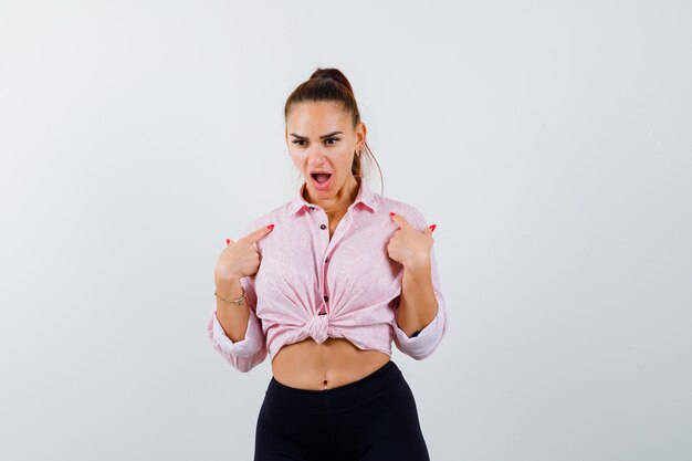 Jeune femme se montrant en chemise, pantalon et l'air choqué. vue de face.