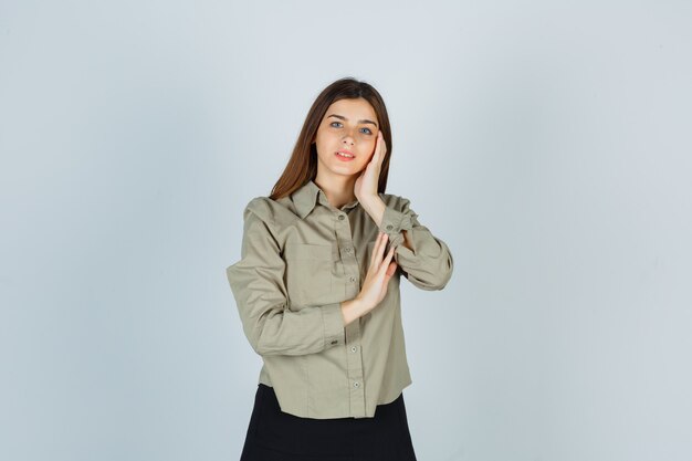 Jeune femme se penchant la joue sur la paume en chemise, jupe et à la gaieté, vue de face.