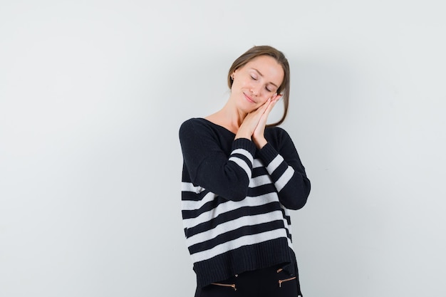 Jeune femme se penchant les mains sur la joue et essayant de dormir en maille rayée et pantalon noir et à la détente