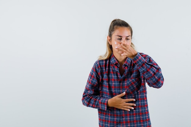 Jeune femme se pinçant le nez en raison d'une mauvaise odeur en chemise à carreaux et à la dégoûté, vue de face.