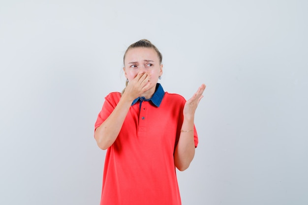 Jeune femme se pinçant le nez en raison d'une mauvaise odeur en t-shirt et à l'air dégoûté