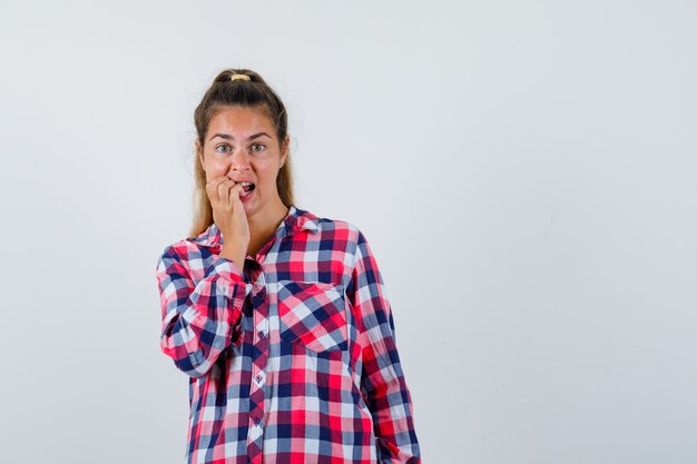 Jeune femme se rongeant les ongles en chemise à carreaux et l'air excité. vue de face.