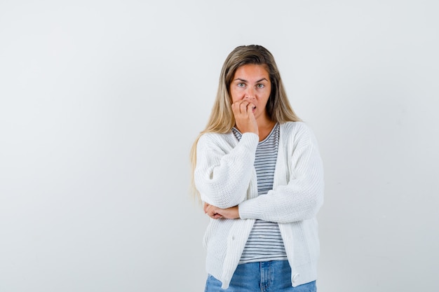 Jeune femme se rongeant les ongles en t-shirt, veste, jeans et regardant pensif, vue de face.