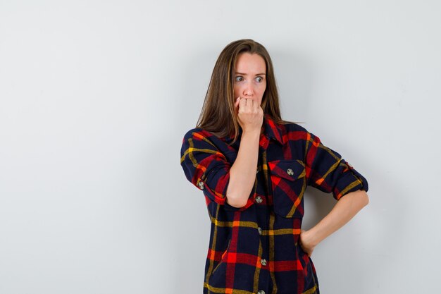 Jeune femme se ronger les ongles émotionnellement en chemise décontractée et à la vue anxieuse, de face.