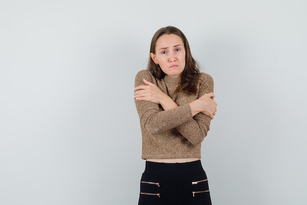 Jeune femme se serrant dans un chemisier, une jupe et l'air inquiet, vue de face.