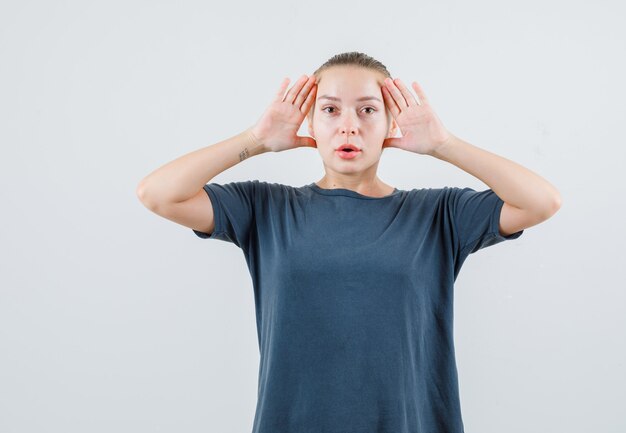 Jeune femme se tenant la main pour voir clairement en t-shirt gris et à la surprise