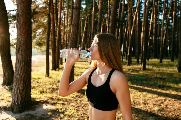 jeune femme séduisante, boire une bouteille d&#39;eau après avoir exercé dans le parc
