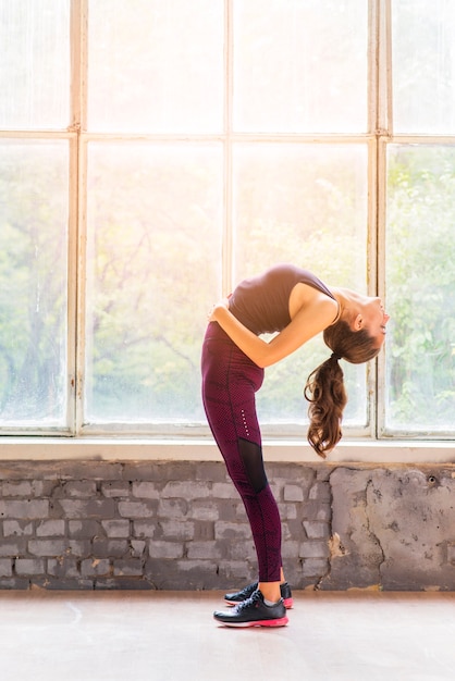 Photo gratuite jeune femme séduisante, debout près de la fenêtre, pratiquant le yoga
