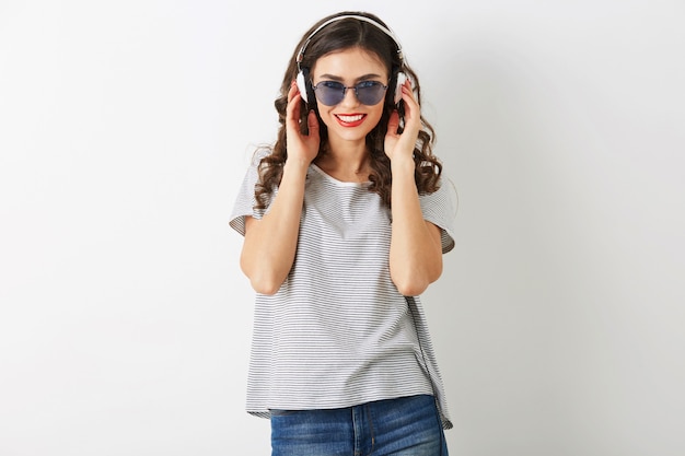 Jeune femme séduisante, écouter de la musique sur des écouteurs, portant des lunettes de soleil, isolé sur fond blanc,
