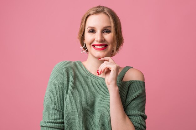 Jeune femme séduisante heureuse souriante, lèvres rouges et ongles vernis, style décontracté, pull vert, émotion joyeuse et positive, modèle posant en studio, isolé, fond rose, regardant à huis clos