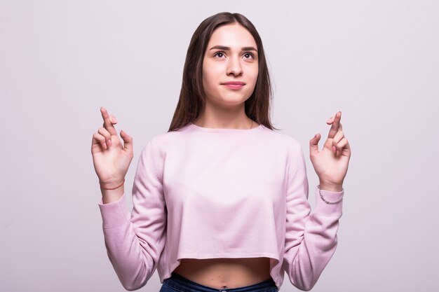 Jeune femme séduisante tient ses doigts croisés, vœux pieux, shoot studio isolé sur fond blanc