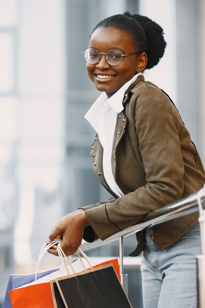 Jeune femme séduisante en veste et tenant beaucoup de colis commerciaux et marchant le long de la rue. Concept de magasinage