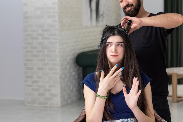 Jeune femme sérieuse assise sur la chaise pendant que Barber se coiffait Photo de haute qualité