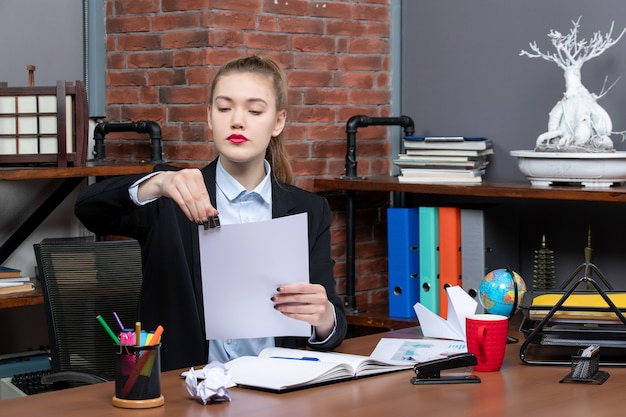 Jeune femme sérieuse assise à une table et lisant ses notes dans un cahier au bureau