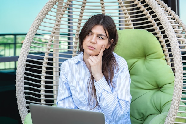 Photo gratuite une jeune femme sérieuse travaille sur un ordinateur portable tout en étant assise dans un hamac
