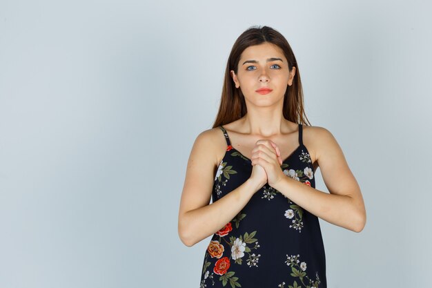 Jeune femme serrant les mains dans un geste de prière en blouse et à l'espoir, vue de face.