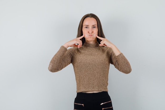 Photo gratuite jeune femme serrant ses joues en chemisier doré