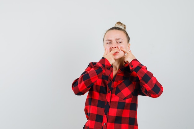 Photo gratuite jeune femme serrant son bouton sur la joue en chemise à carreaux, vue de face.