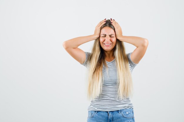 Jeune femme serrant la tête avec les mains en t-shirt et à la recherche d'anxiété. vue de face.