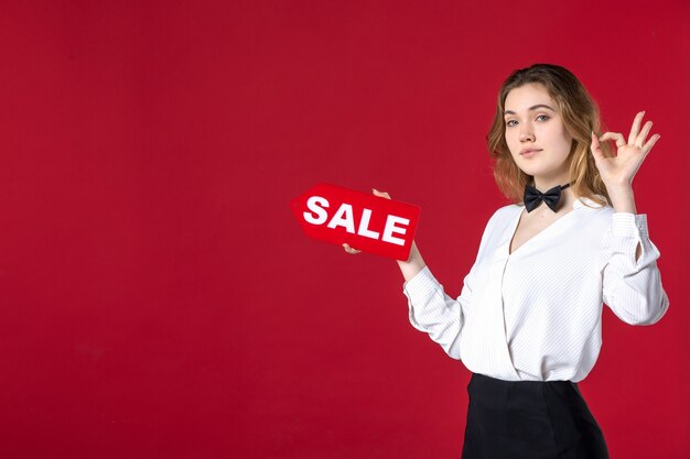 jeune femme serveur papillon sur le cou et tenant l'icône de vente faisant un geste de lunettes sur fond rouge