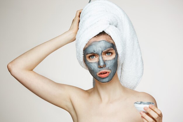 Jeune femme en serviette sur la tête avec masque facial fronçant les sourcils. Beauté et soin.