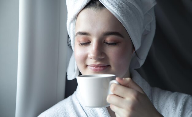 Une jeune femme avec une serviette sur la tête avec une tasse de café le matin