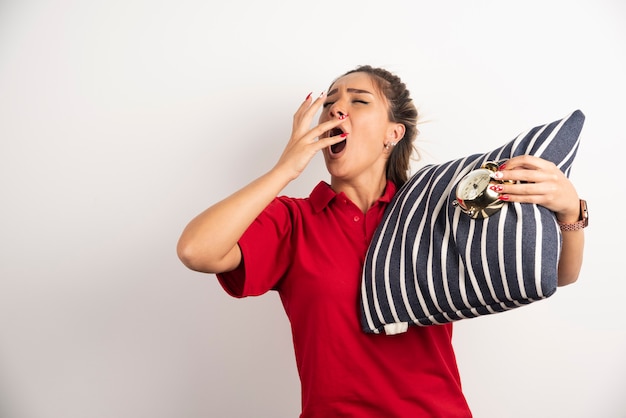 Jeune femme en short rouge montrant un réveil et tenant un oreiller.