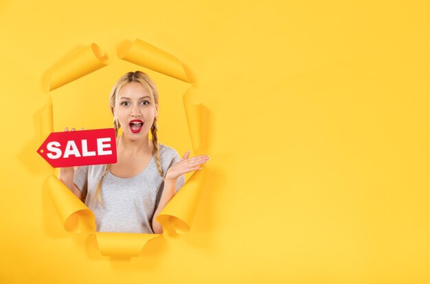 Jeune femme avec signe d'inscription de vente sur un fond de papier jaune déchiré facial shopping intérieur