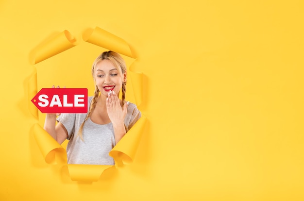 Photo gratuite jeune femme avec signe d'inscription de vente sur fond de papier jaune déchiré shopping à l'intérieur du visage