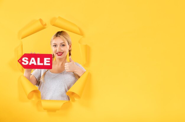 Jeune femme avec signe d'inscription de vente sur fond de papier jaune déchiré shopping intérieur