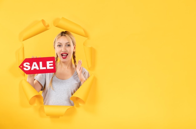Jeune femme avec signe d'inscription de vente sur fond de papier jaune déchiré shopping soins du visage à l'intérieur