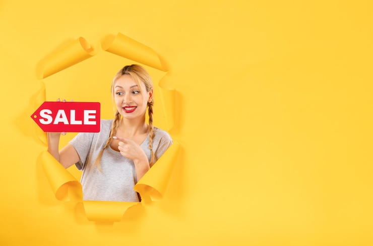 Photo gratuit jeune femme avec signe d'inscription de vente à la recherche du visage de fond de papier jaune déchiré