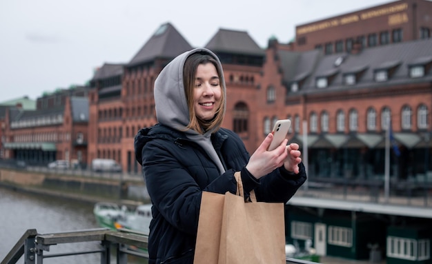 Une jeune femme avec un smartphone et un sac à provisions dans la ville