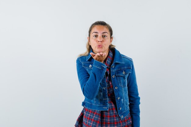 Jeune femme soufflant baiser de l'air avec des lèvres boudeuses en chemise, veste et à la jolie vue de face.