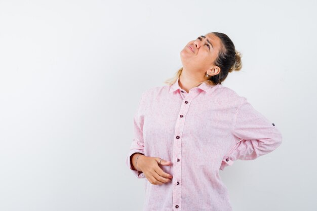 Jeune femme souffrant de maux de dos en chemise rose et à la fatigue