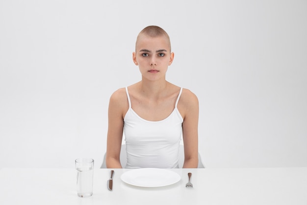 Photo gratuite jeune femme souffrant d'un trouble de l'alimentation assise à la table