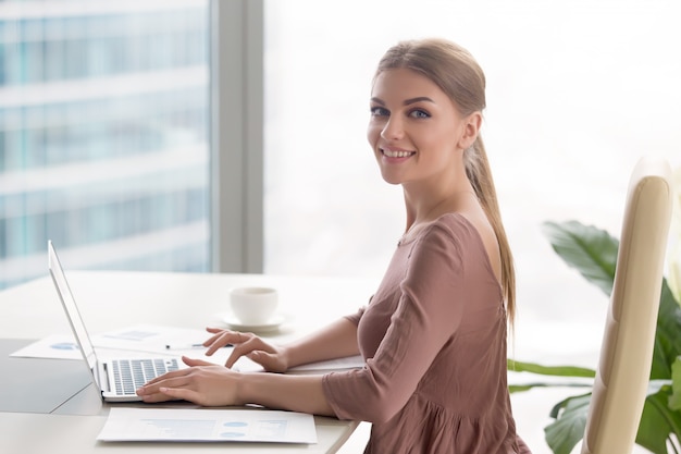 Jeune femme souriante assise au bureau en regardant la caméra