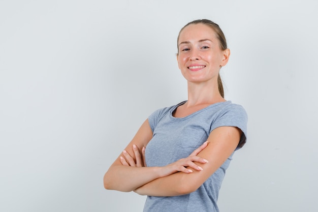 Jeune femme souriante avec les bras croisés en t-shirt gris et regardant confiant, vue de face.