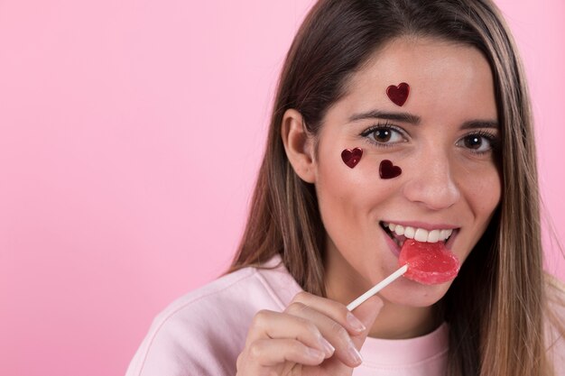 Jeune femme souriante avec coeurs d&#39;ornement sur le visage et la sucette