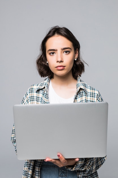 Jeune femme souriante heureuse dans des vêtements décontractés tenant un ordinateur portable et l'envoi de courrier électronique à sa meilleure amie isolée sur fond gris