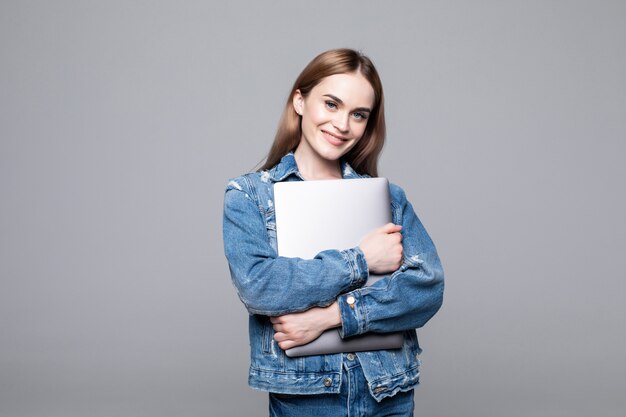 Jeune femme souriante heureuse dans des vêtements décontractés tenant un ordinateur portable et envoyer un e-mail à son meilleur ami isolé sur mur gris